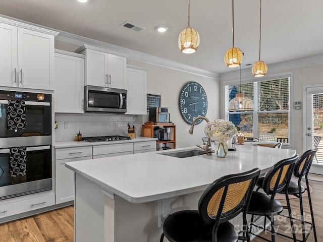 kitchen with a center island with sink, visible vents, ornamental molding, a sink, and appliances with stainless steel finishes