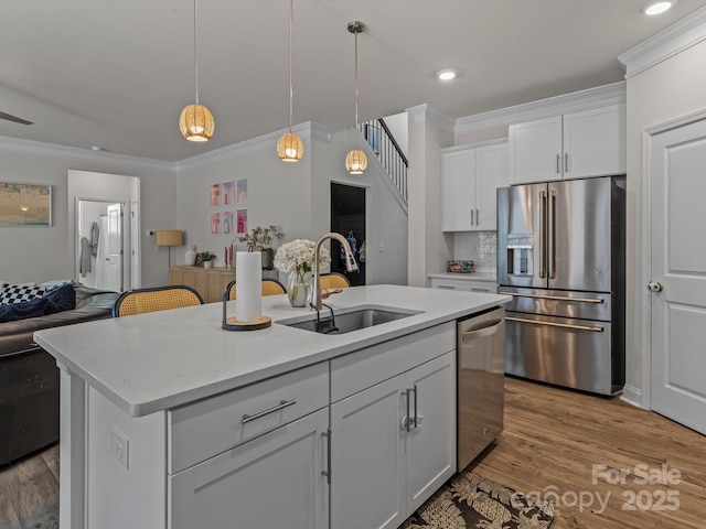 kitchen with open floor plan, ornamental molding, appliances with stainless steel finishes, and a sink