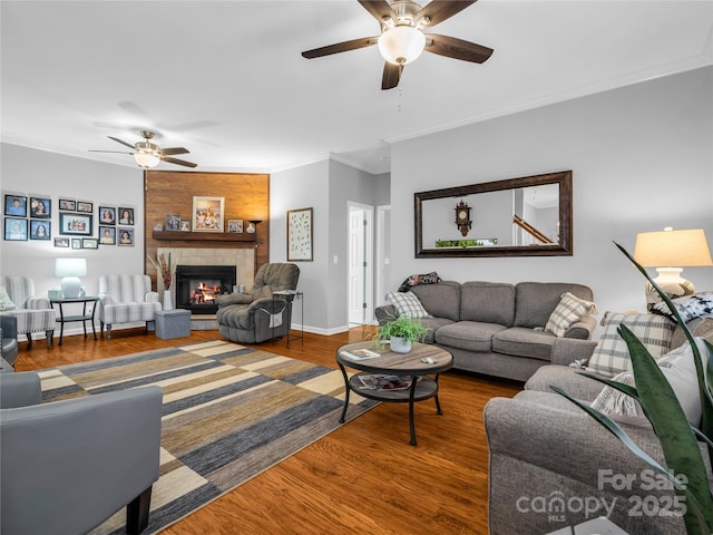 living area with a fireplace, crown molding, a ceiling fan, and wood finished floors
