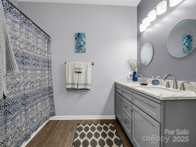 full bathroom featuring double vanity, wood finished floors, baseboards, and a sink