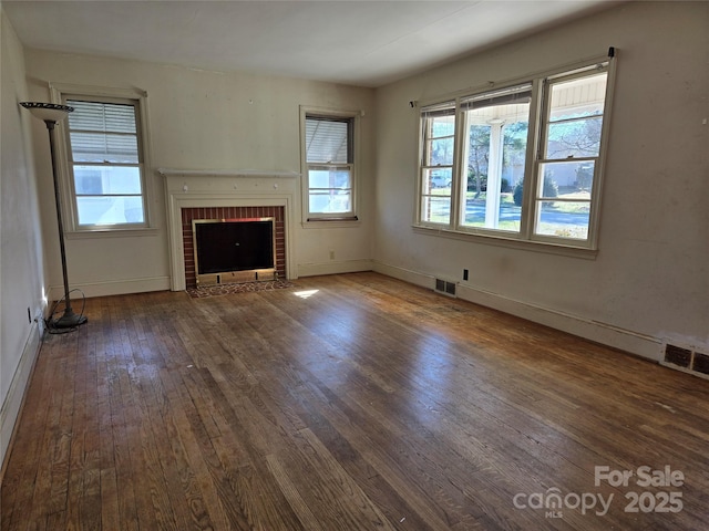 unfurnished living room featuring baseboards, visible vents, wood-type flooring, and a brick fireplace