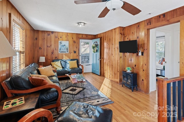 living area featuring light wood finished floors, wood walls, a wood stove, and a ceiling fan