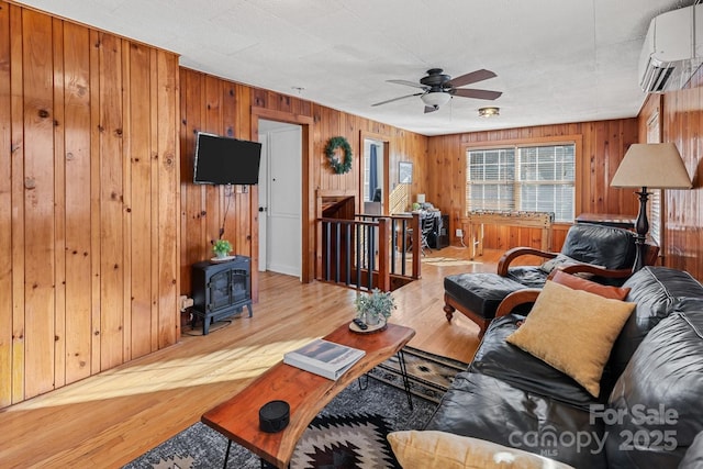 living room featuring a wall mounted AC, a wood stove, ceiling fan, and wood finished floors