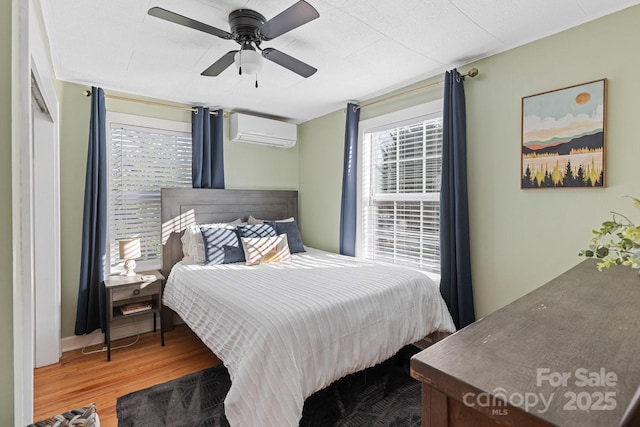 bedroom with ceiling fan, multiple windows, wood finished floors, and a wall unit AC