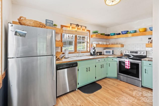 kitchen with open shelves, light wood-style flooring, a sink, appliances with stainless steel finishes, and backsplash