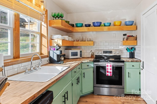 kitchen featuring white microwave, stainless steel electric stove, a sink, and open shelves