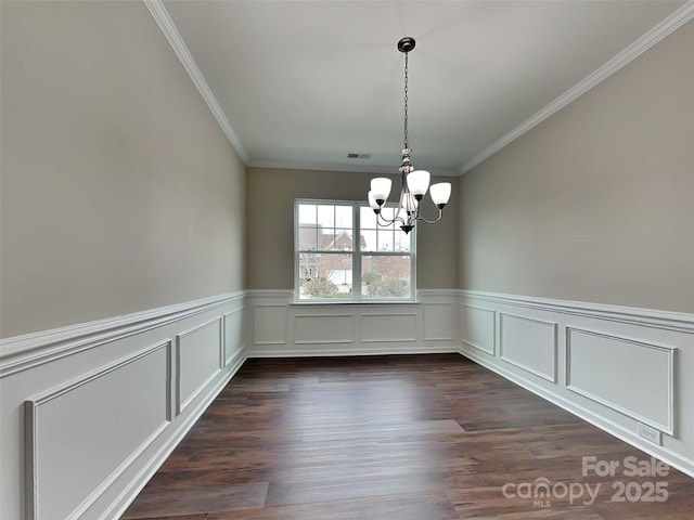 unfurnished dining area with a wainscoted wall, visible vents, dark wood-style flooring, ornamental molding, and a chandelier