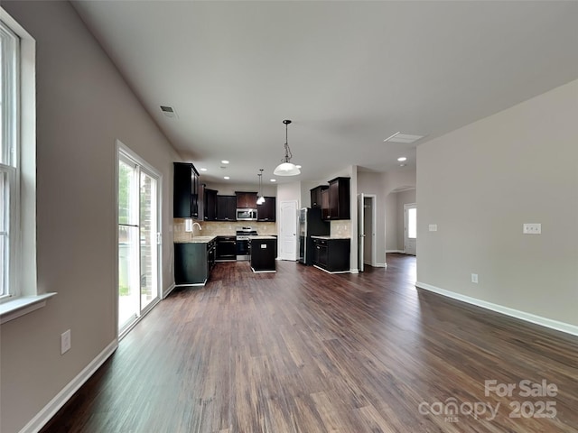 unfurnished living room with plenty of natural light, dark wood-style floors, arched walkways, and baseboards