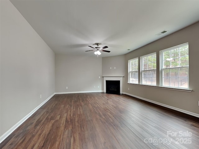 unfurnished living room with visible vents, a fireplace with flush hearth, dark wood-style floors, baseboards, and ceiling fan