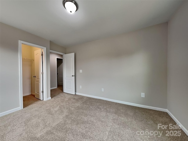 unfurnished bedroom featuring a walk in closet, carpet flooring, and baseboards