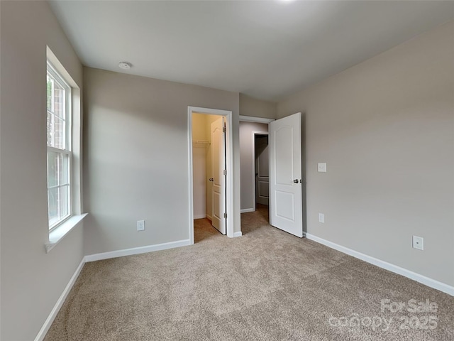 unfurnished bedroom featuring a walk in closet, baseboards, carpet floors, and a closet