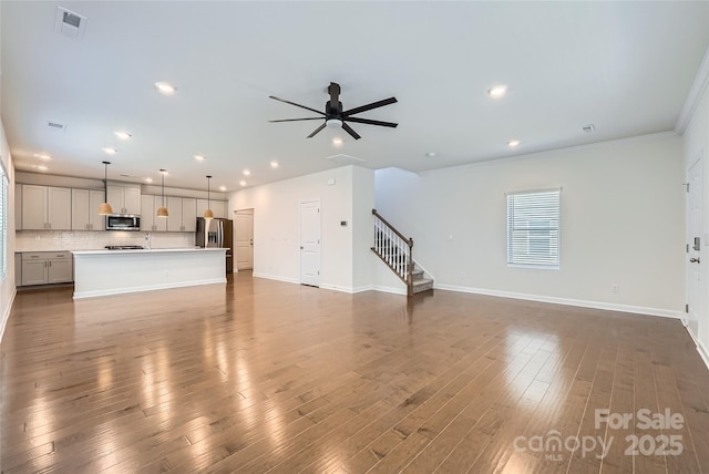 unfurnished living room featuring a ceiling fan, stairs, baseboards, and wood finished floors