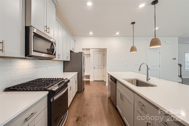 kitchen with wood finished floors, a sink, decorative backsplash, light countertops, and stainless steel appliances