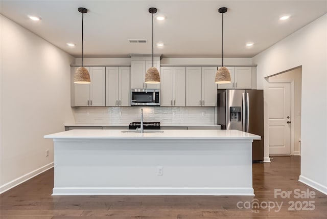 kitchen featuring backsplash, appliances with stainless steel finishes, light countertops, and a kitchen island with sink