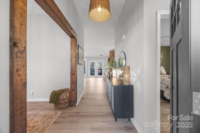 hallway featuring light wood-type flooring, baseboards, and beam ceiling