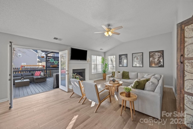 living area featuring wood finished floors, visible vents, a ceiling fan, lofted ceiling, and a fireplace