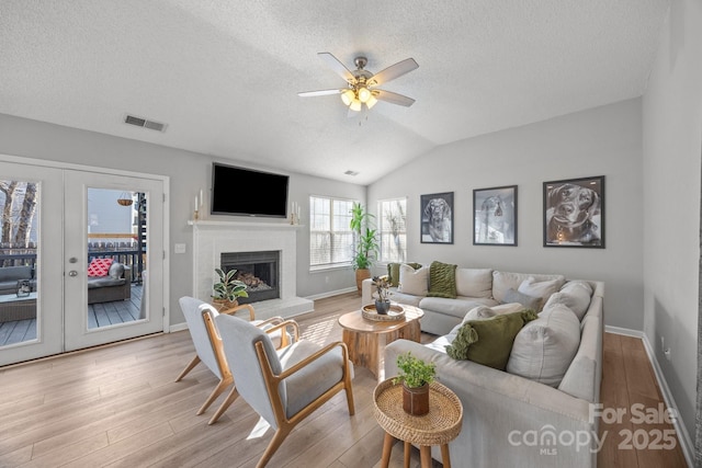 living room featuring visible vents, a brick fireplace, lofted ceiling, wood finished floors, and a ceiling fan