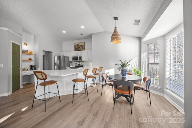 dining area with visible vents, baseboards, light wood-style flooring, and vaulted ceiling