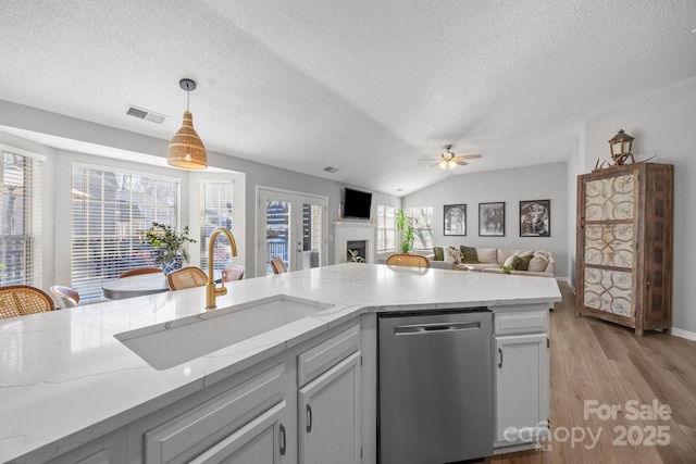 kitchen with visible vents, a sink, stainless steel dishwasher, light wood-style floors, and a fireplace