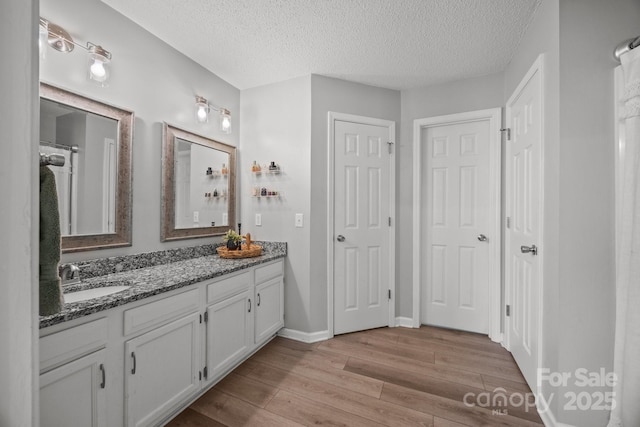 full bath featuring wood finished floors, baseboards, double vanity, a sink, and a textured ceiling