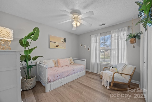 bedroom featuring visible vents, light wood-style flooring, a textured ceiling, and a ceiling fan