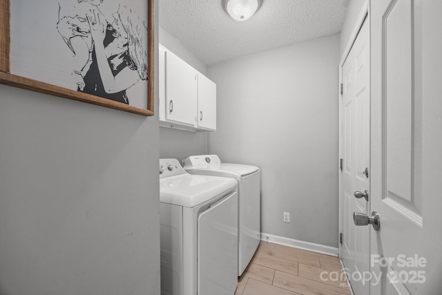 washroom featuring baseboards, cabinet space, light wood-style floors, a textured ceiling, and washer and clothes dryer