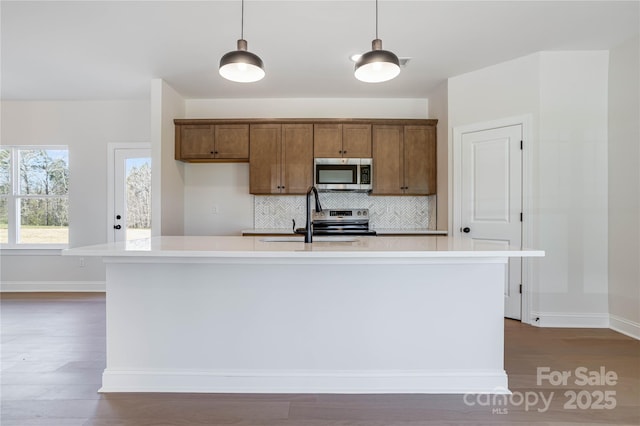 kitchen with a sink, backsplash, appliances with stainless steel finishes, light countertops, and hanging light fixtures