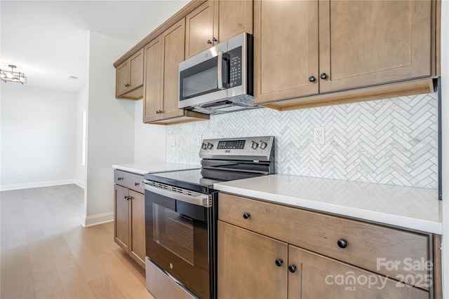 kitchen with light wood finished floors, backsplash, appliances with stainless steel finishes, and light countertops