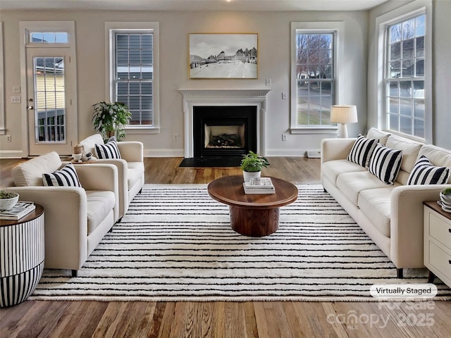 living area featuring a fireplace with flush hearth, baseboards, and wood finished floors