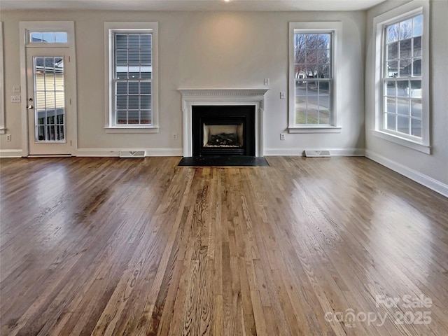 unfurnished living room with a fireplace with flush hearth, wood finished floors, visible vents, and baseboards