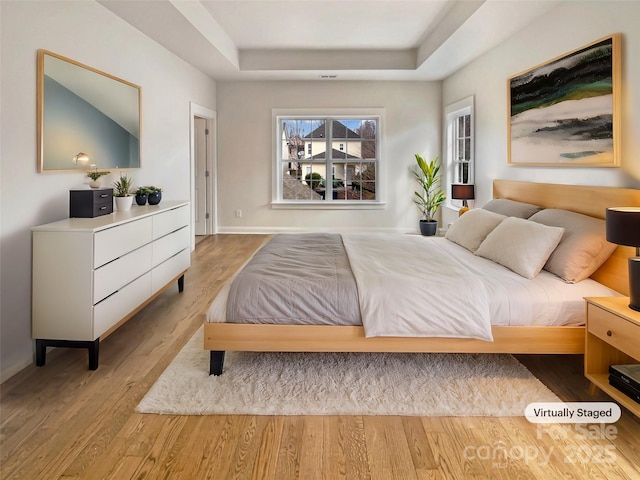 bedroom with a tray ceiling, wood finished floors, and baseboards