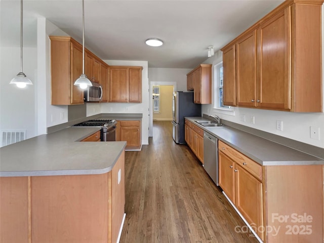 kitchen featuring visible vents, a sink, wood finished floors, a peninsula, and appliances with stainless steel finishes