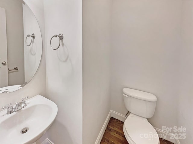 half bathroom featuring a sink, baseboards, toilet, and wood finished floors