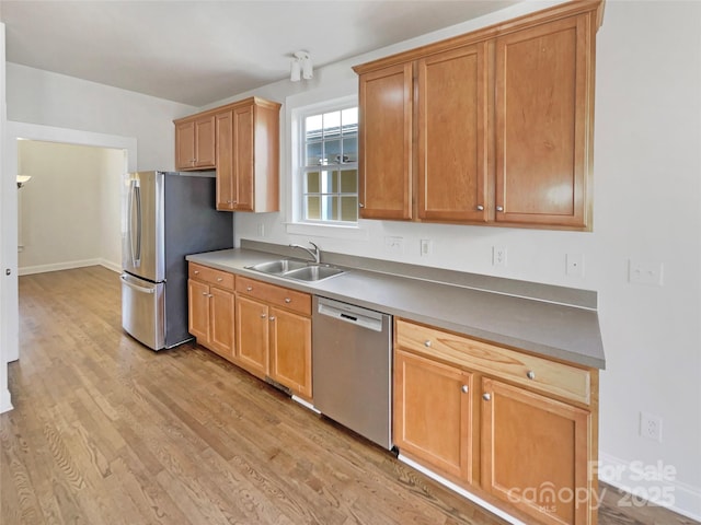 kitchen with a sink, baseboards, light wood-type flooring, and stainless steel appliances