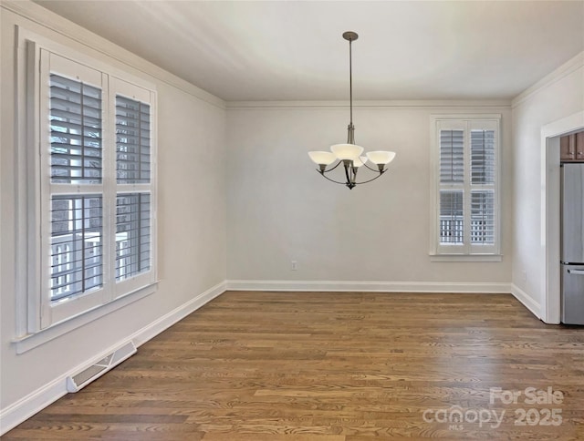 unfurnished dining area featuring an inviting chandelier, wood finished floors, visible vents, and baseboards