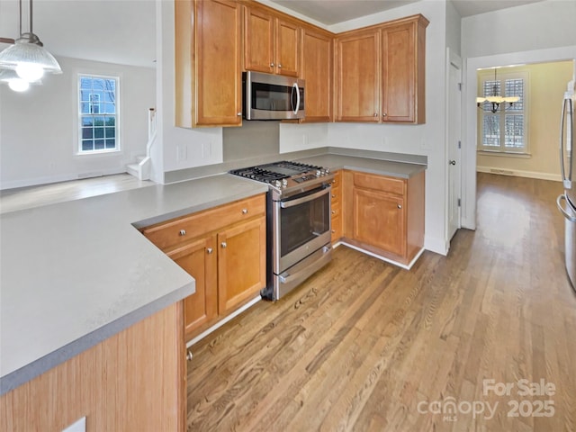 kitchen with light wood-type flooring, an inviting chandelier, stainless steel appliances, pendant lighting, and brown cabinets