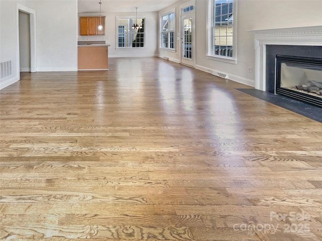 unfurnished living room featuring an inviting chandelier, a fireplace with flush hearth, wood finished floors, and baseboards