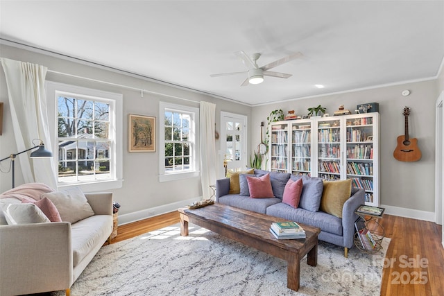 living area featuring crown molding, wood finished floors, baseboards, and ceiling fan