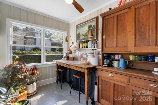 interior space featuring tile patterned flooring, ornamental molding, brown cabinets, wood counters, and a ceiling fan