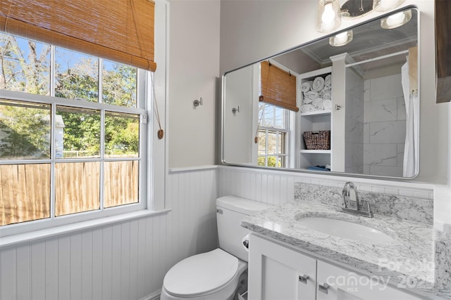 bathroom with wainscoting, toilet, vanity, and a healthy amount of sunlight