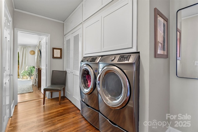 laundry room with wood finished floors, washing machine and dryer, cabinet space, and ornamental molding