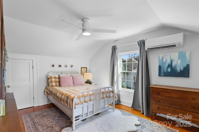 bedroom with a ceiling fan, lofted ceiling, a wall unit AC, and wood finished floors