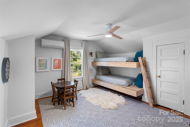 bedroom featuring an AC wall unit, wood finished floors, baseboards, and vaulted ceiling