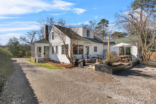 exterior space with a shingled roof, a deck, a chimney, and a sunroom