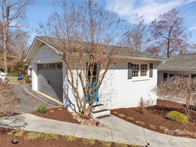 ranch-style home with a garage, brick siding, driveway, and a shingled roof