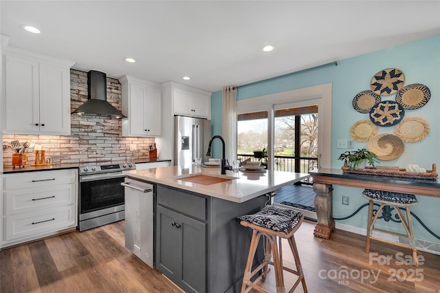 kitchen with dark wood-type flooring, gray cabinetry, a breakfast bar, appliances with stainless steel finishes, and wall chimney exhaust hood