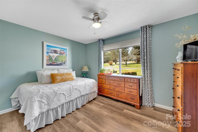 bedroom featuring a ceiling fan, wood finished floors, baseboards, and a textured ceiling