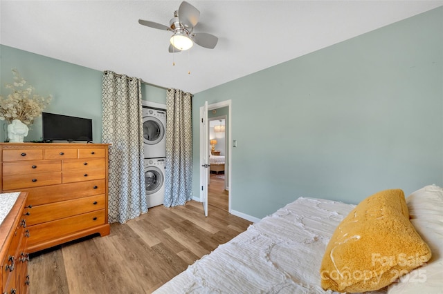 bedroom featuring a ceiling fan, stacked washer and dryer, wood finished floors, and baseboards