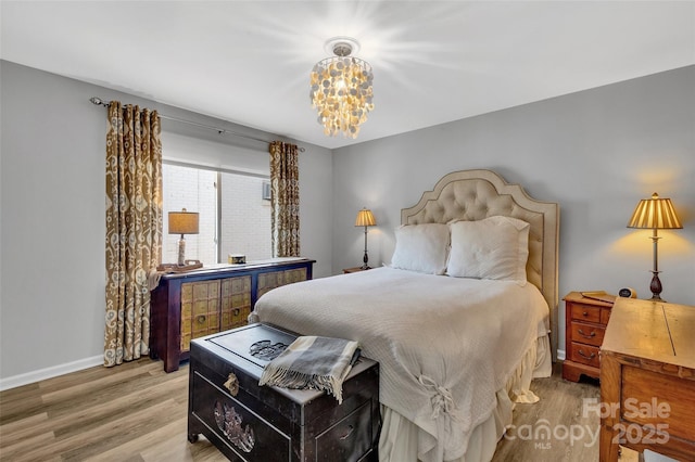 bedroom featuring baseboards, light wood-type flooring, and an inviting chandelier