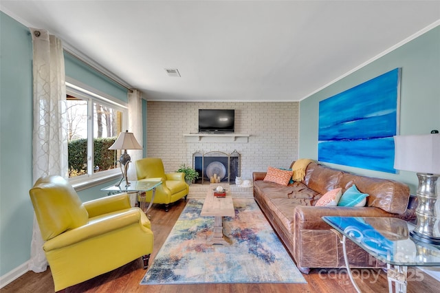 living room featuring visible vents, a brick fireplace, crown molding, baseboards, and wood finished floors